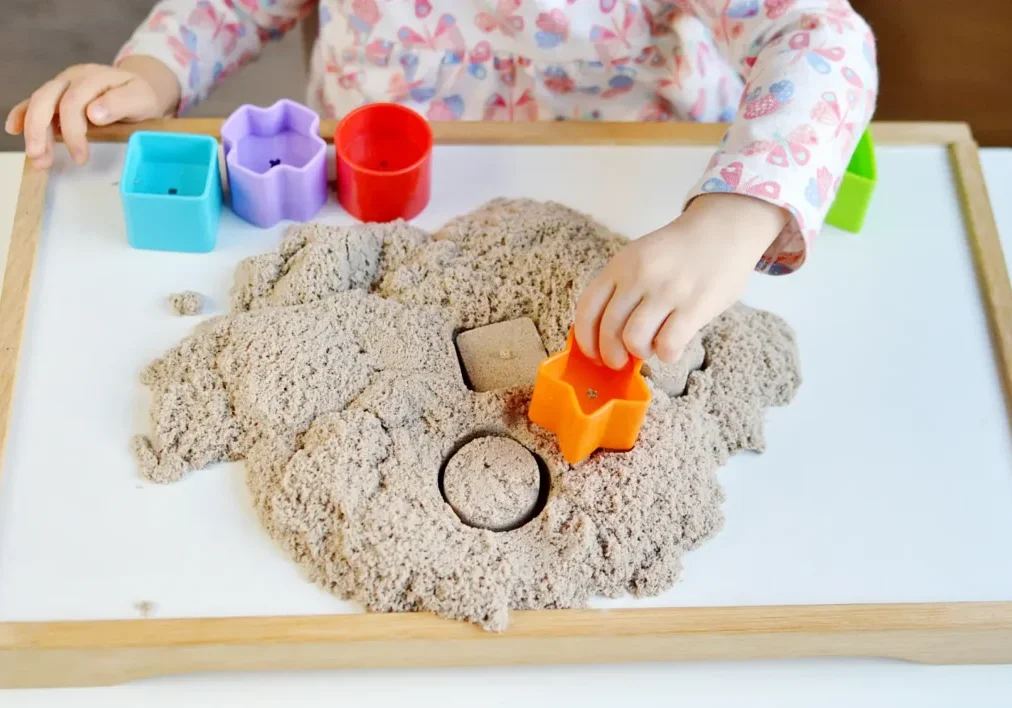 Child shaping kinetic sand with star mold